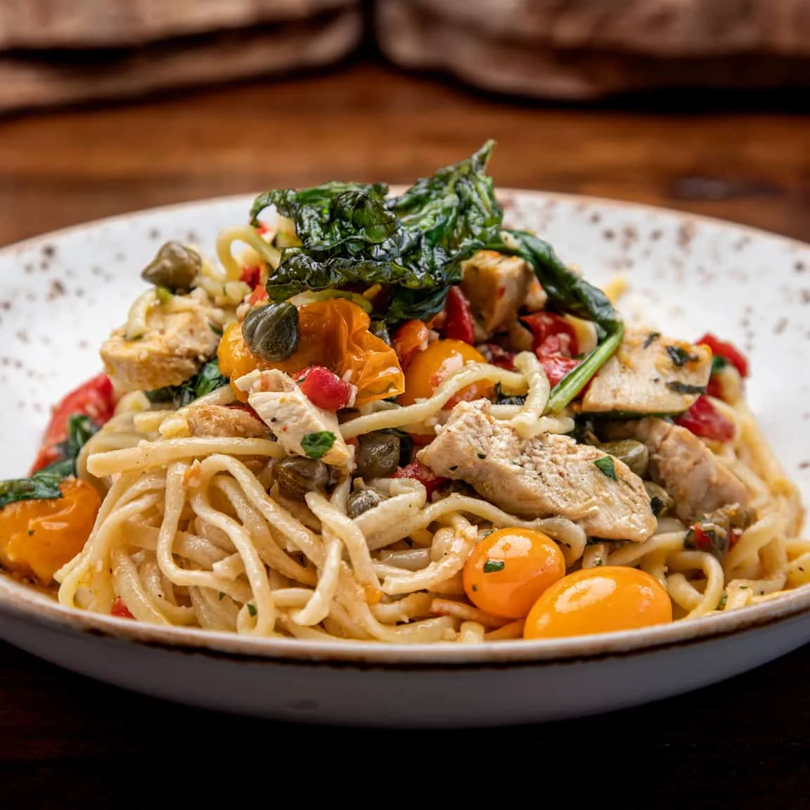 A close-up of a dish of pasta with chicken and fresh basil leaves on top