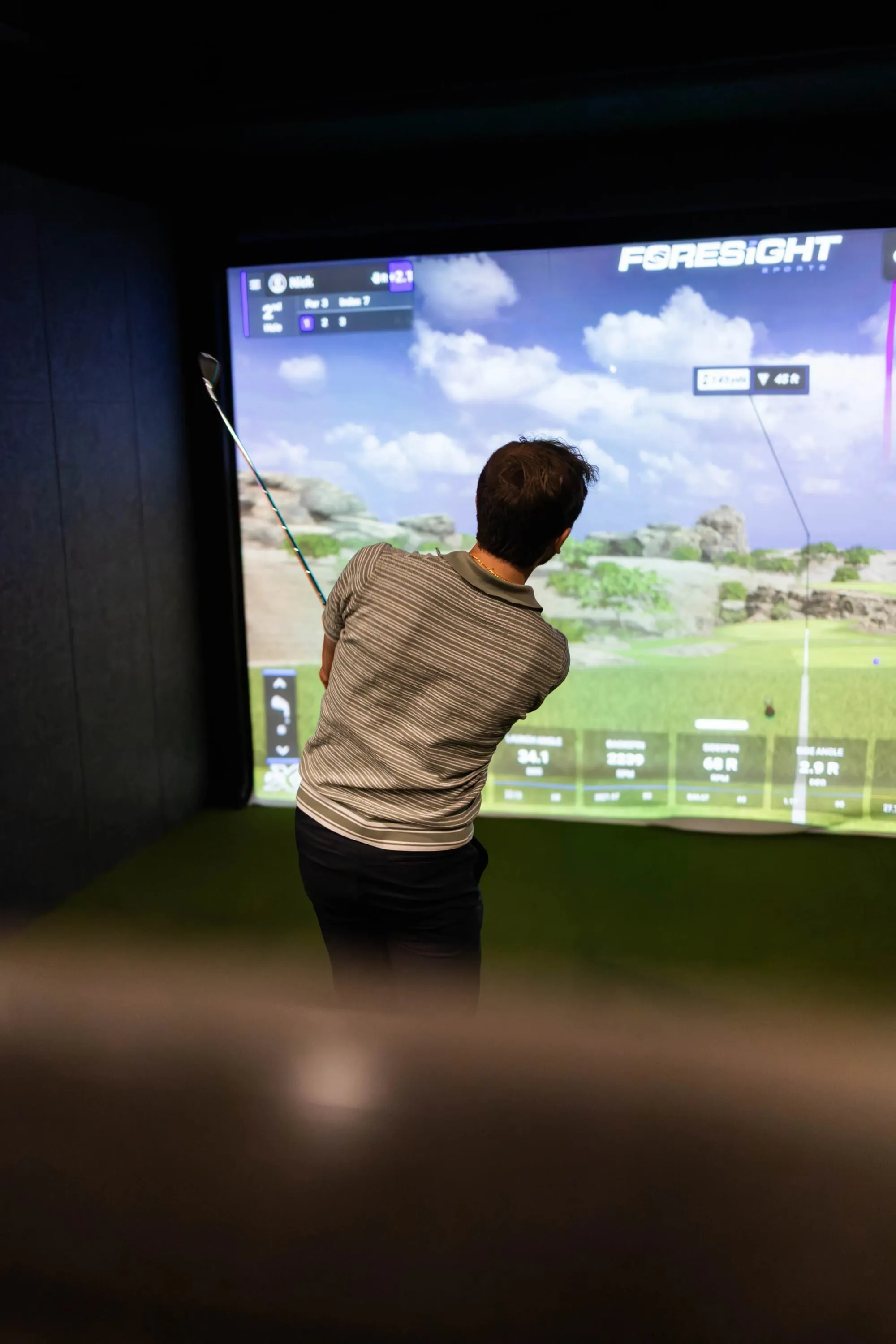 A man is playing a golf simulator on a large projector screen