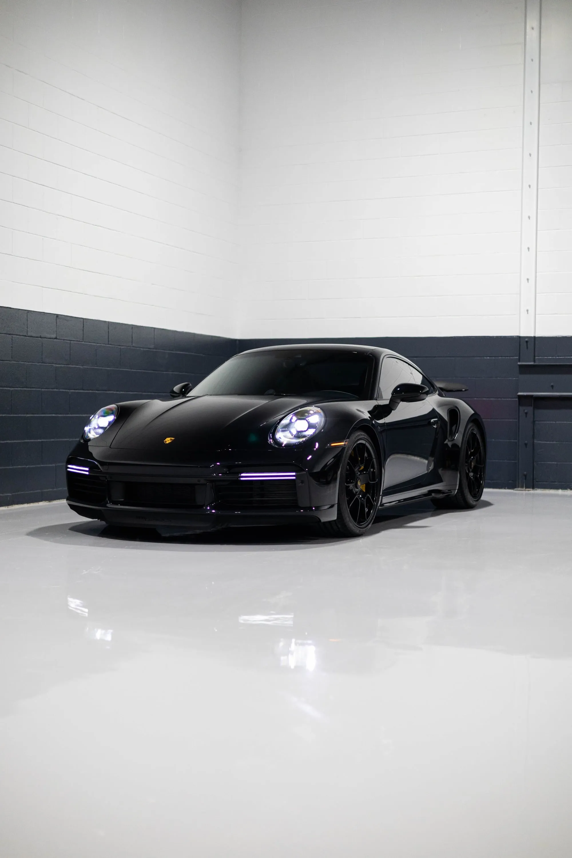 A black Porsche 911 Turbo S parked in a garage with a neon light