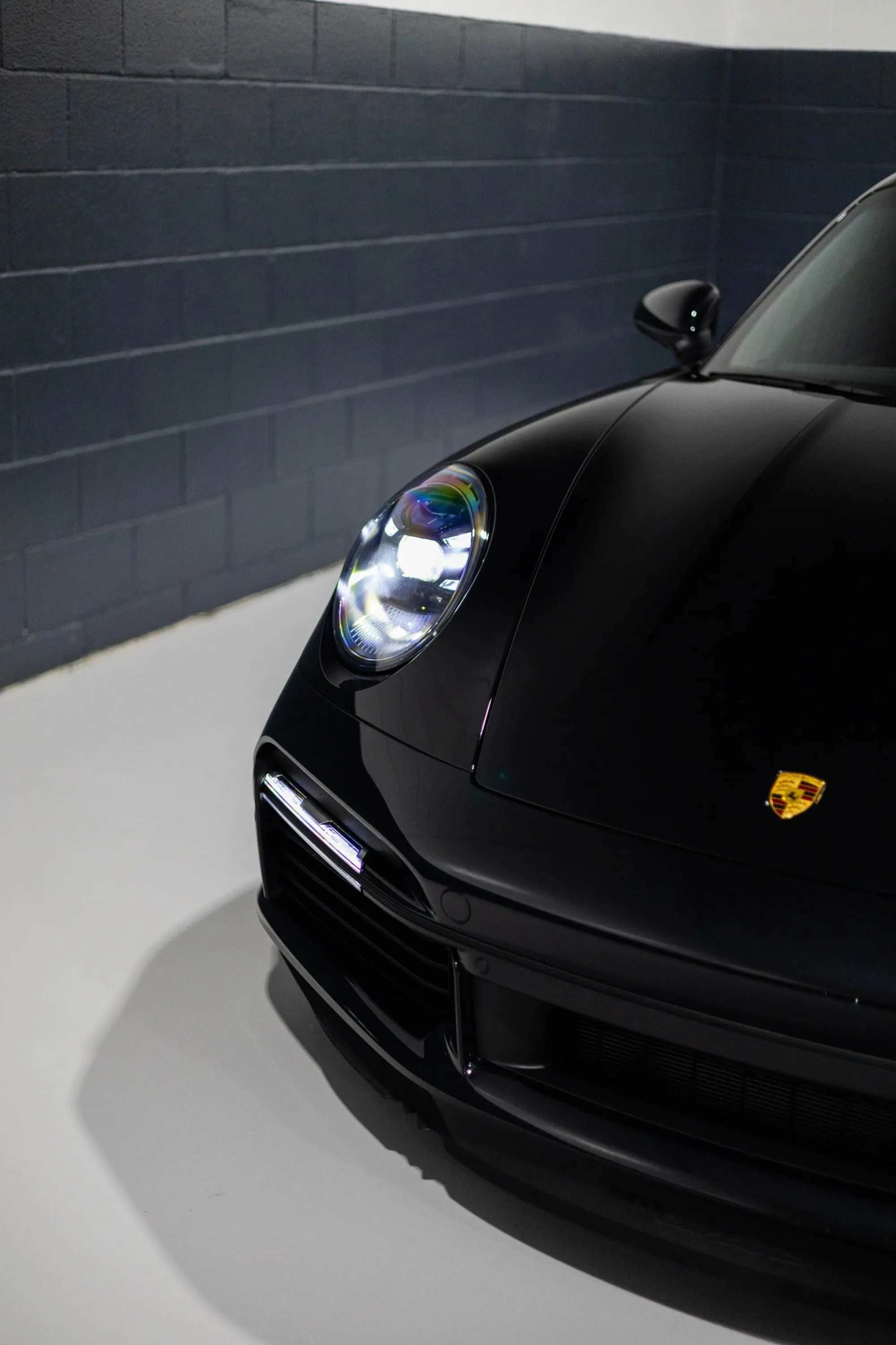 A black sports car parked in a garage, with emphasis on the headlight